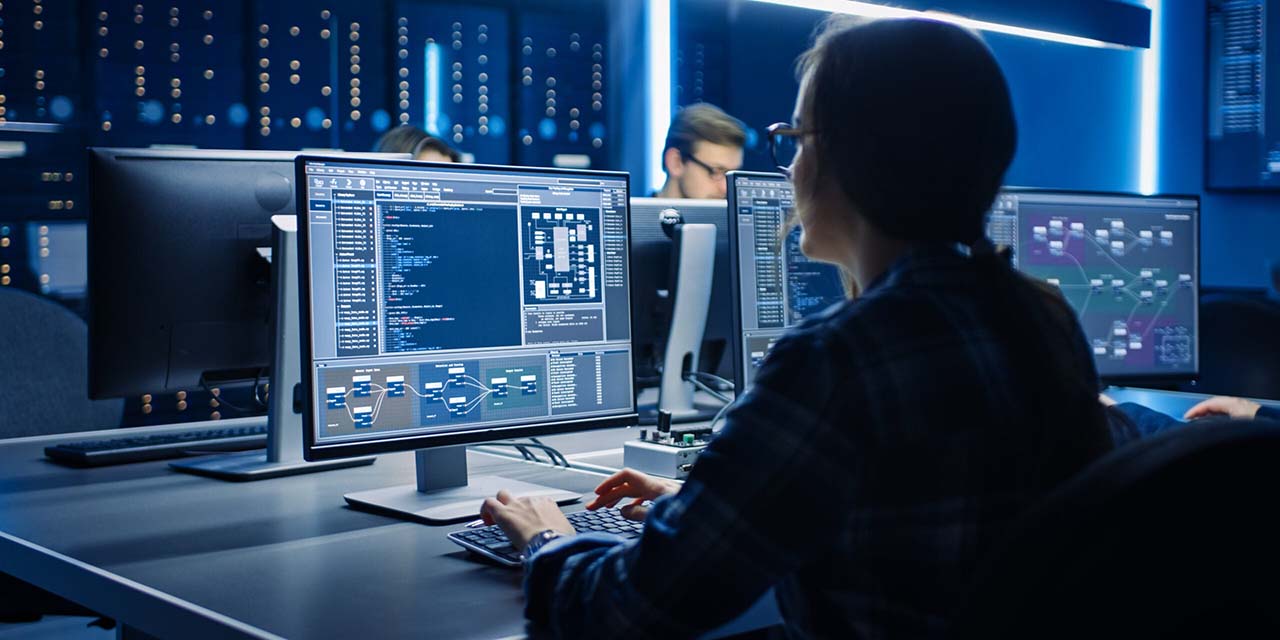 Person working on multiple monitors displaying code and data charts in a dimly lit, high-tech AI research lab