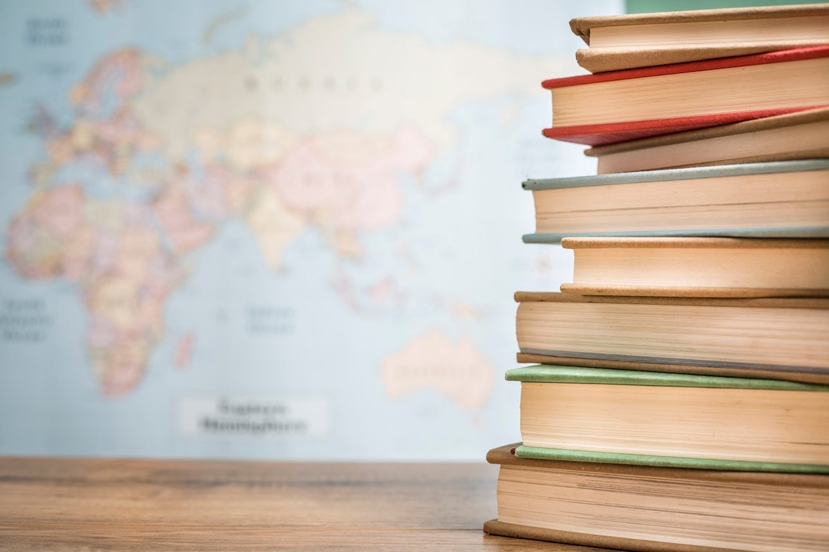 Back to school. Textbooks stacked on wooden school desk in front of world map. Classroom setting.