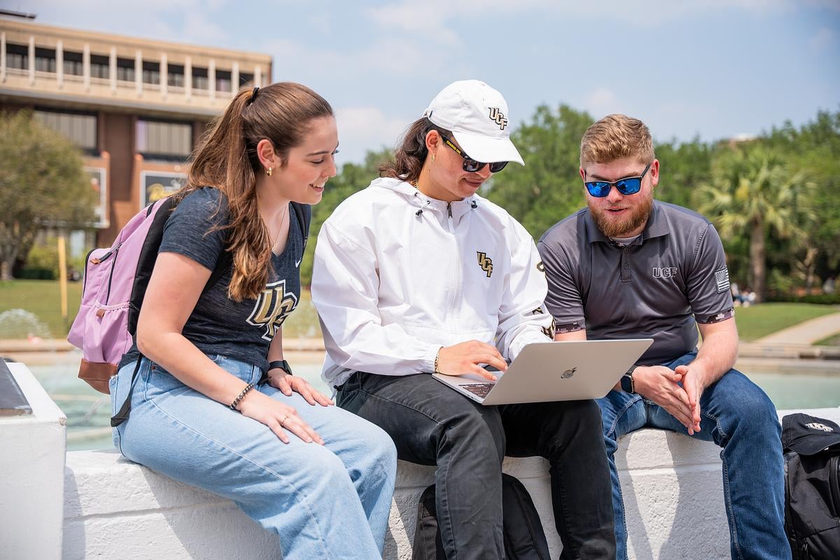 Three students sitting outside and looking at a laptop