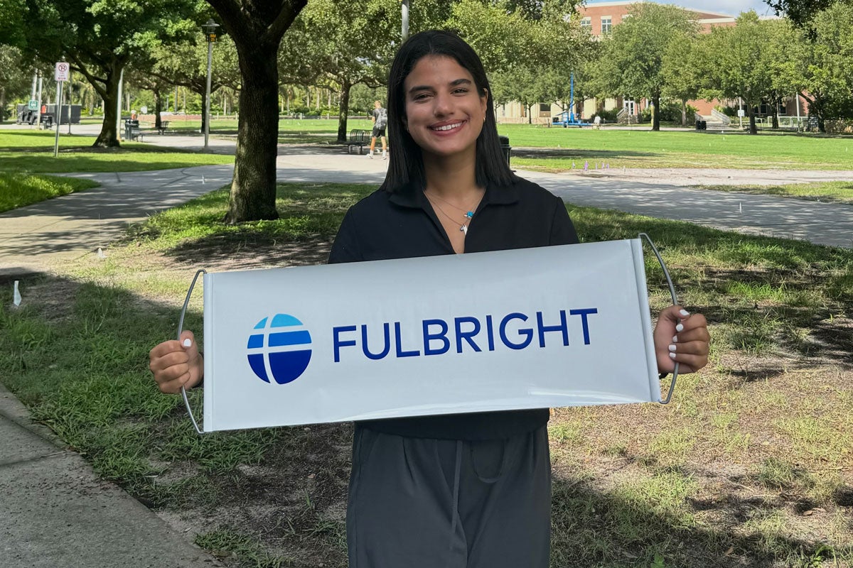 Sarah Al Asmar holding a sign that has a Fulbright sign