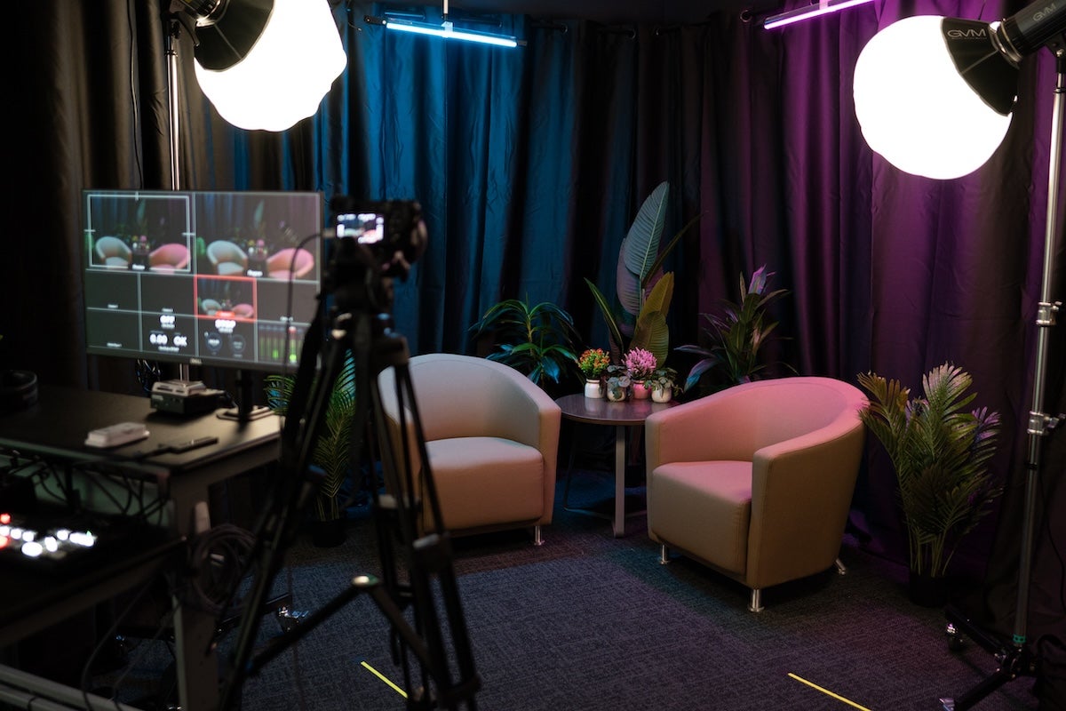 A studio setup with chairs, lighting, podcast equipment and a camera.