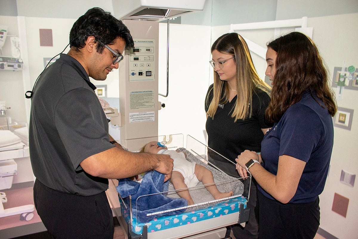 three people examine a baby manikin in a simulated NICU unit