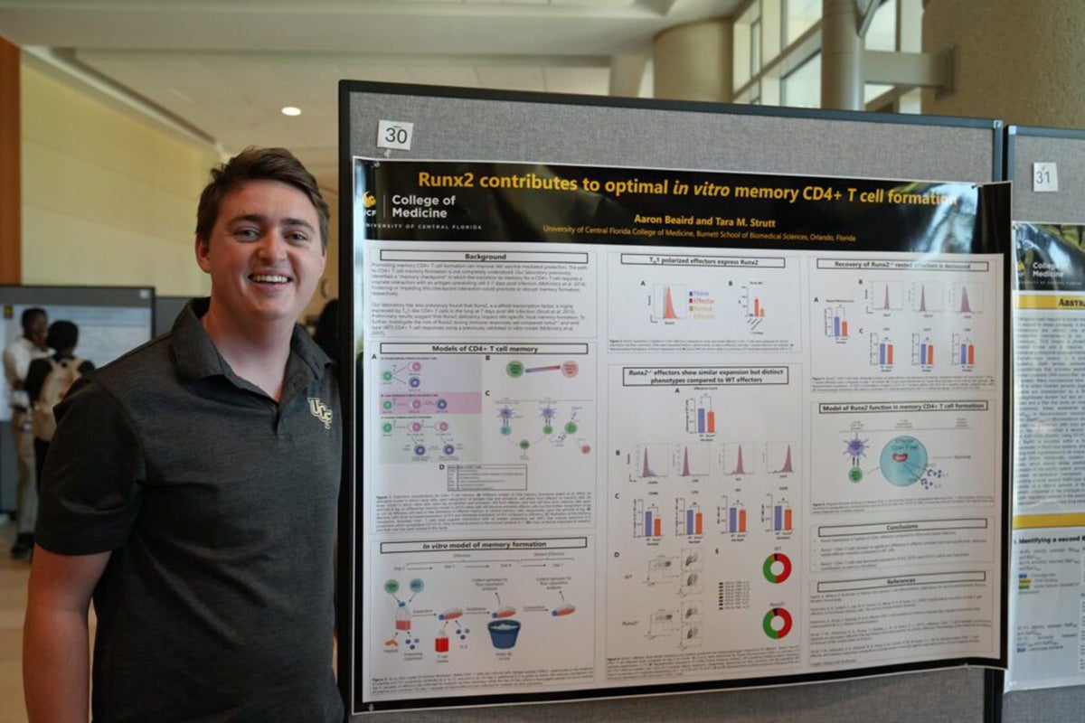 Student poses for a photo next to a research poster