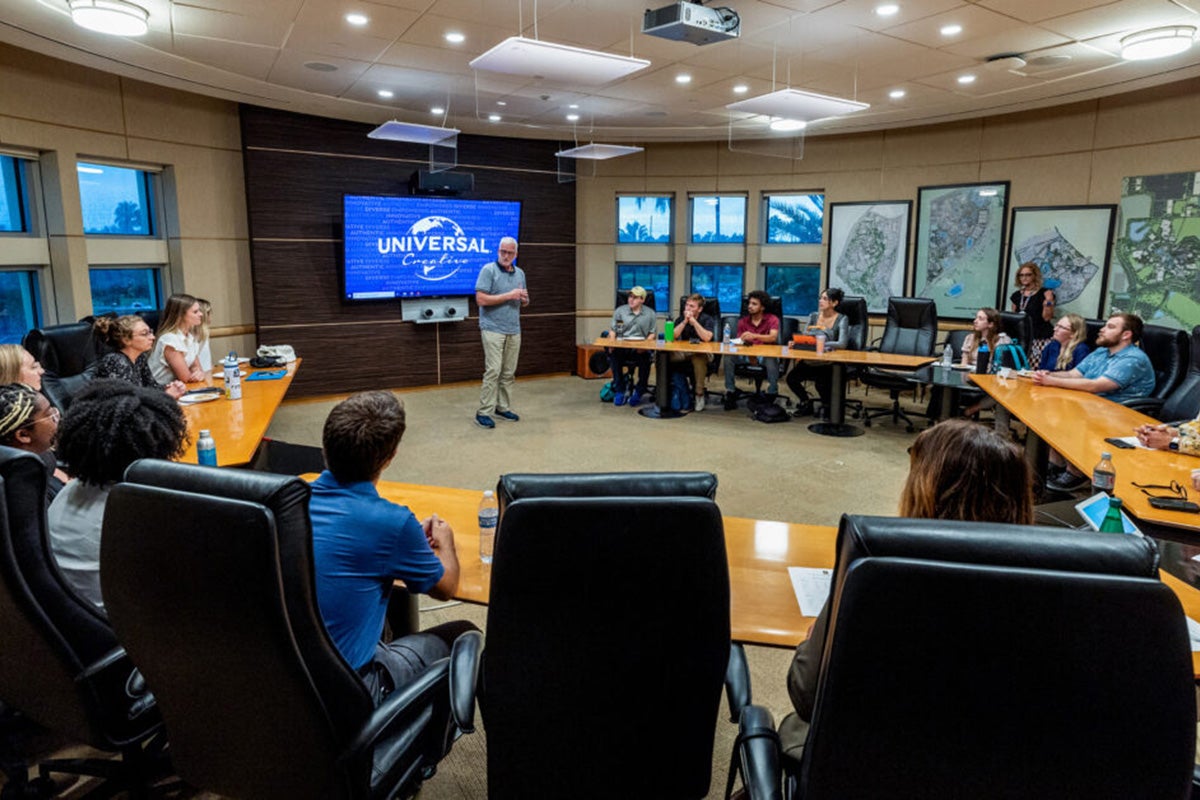 Male stands in front of a TV delivering a presentation to a panel of Universal Creative leaders