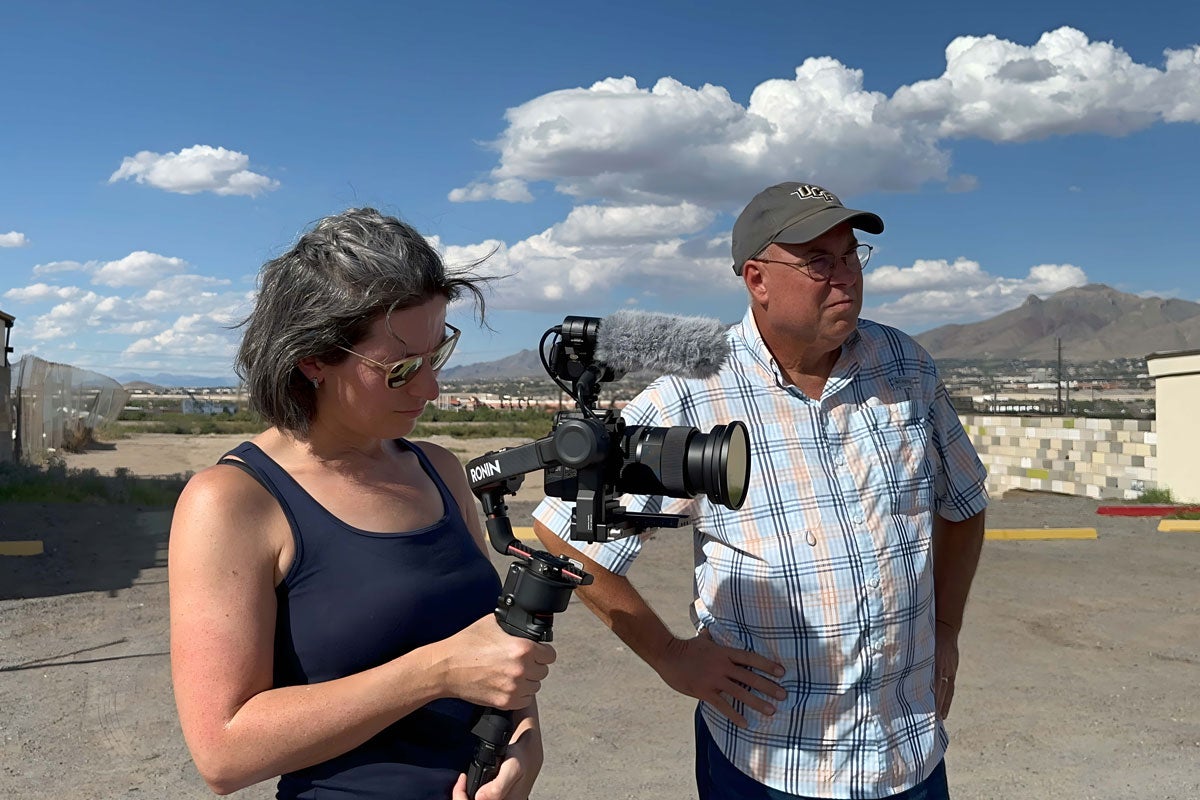 A woman using a video camera and a man standing nearby