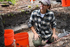 UCF anthropology student kneels in dirt digging up artifacts