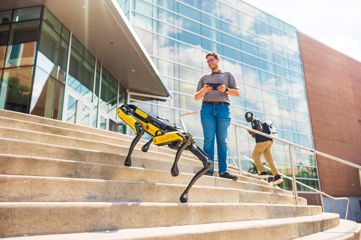 A student guides a dog-like robot up the steps of John C. Hitt Library located at UCF's main campus