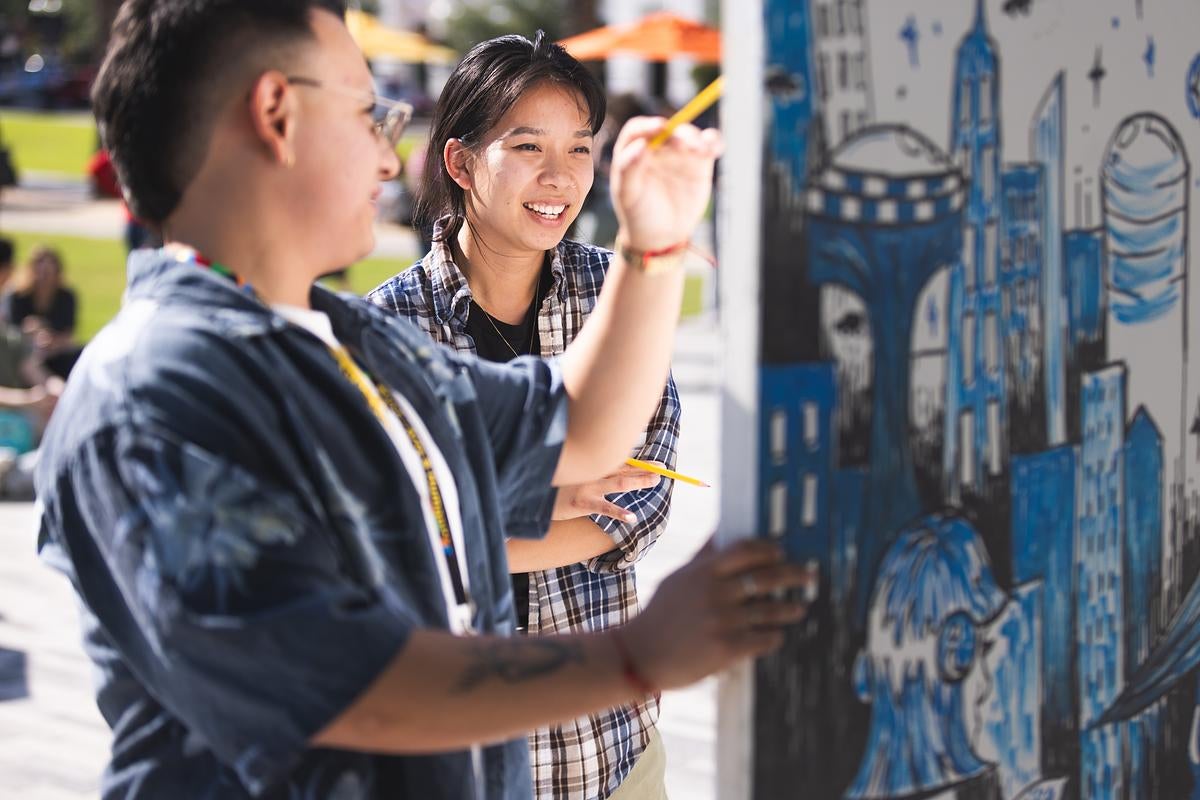 Two people draw artwork on a canvas with markers during UCF's Celebrates the Arts Creative Clash event