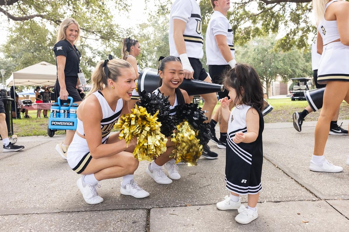 Two cheerleaders interact with a young UCF fan