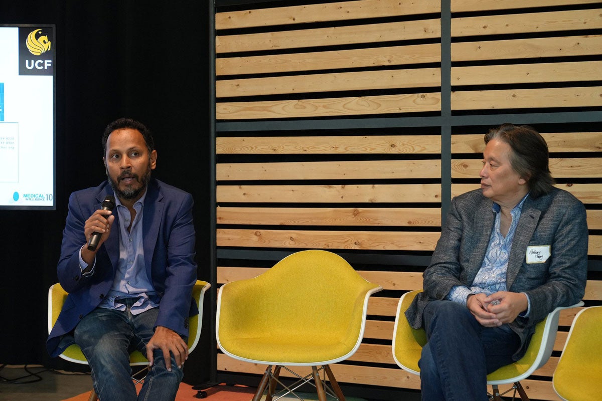 Two men sitting while one speaks and holds a microphone