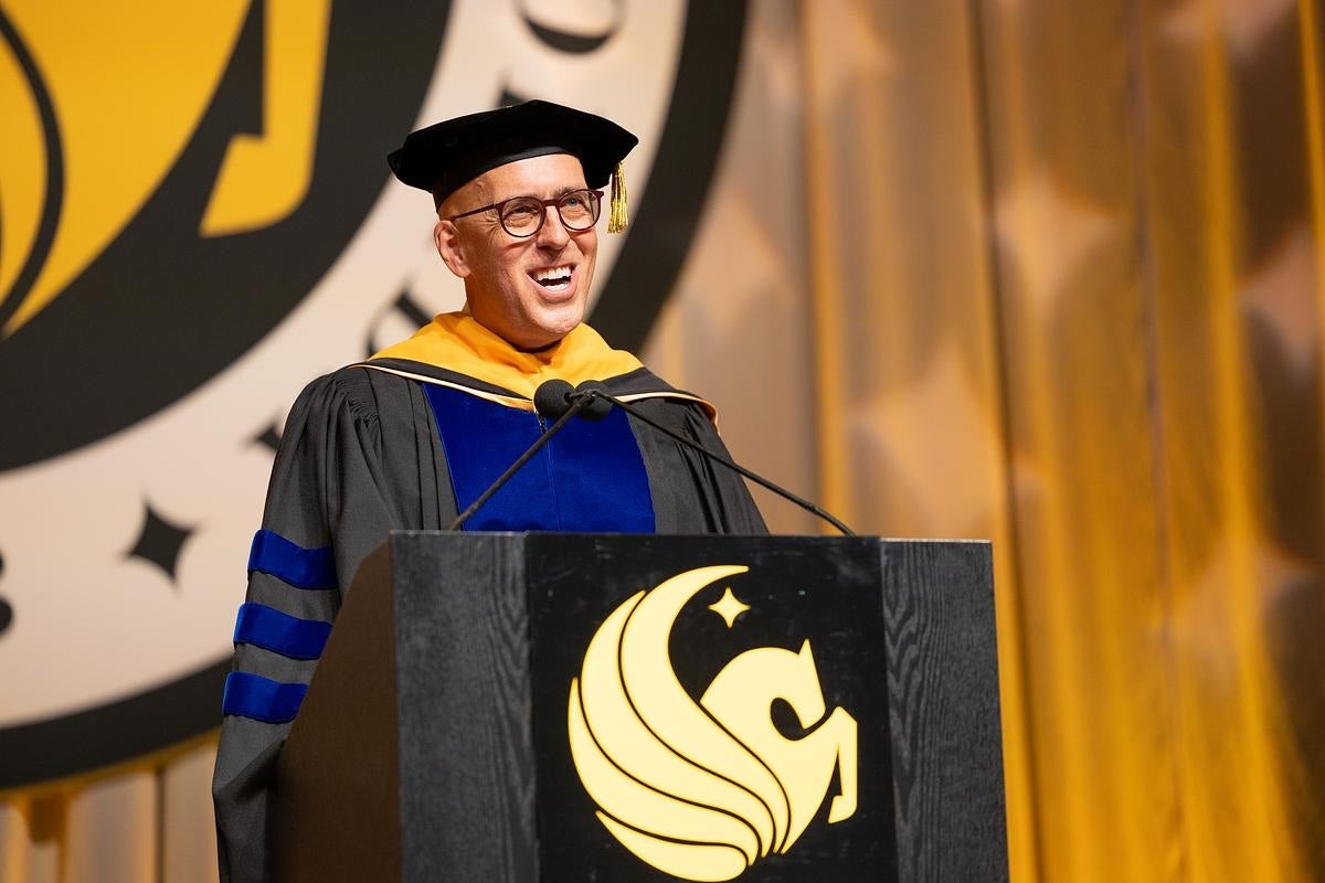 Thad Seymour Jr wearing a cap and gown and speaking at a commencement podium