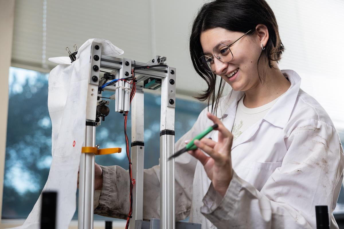 Student wearing a white lab coat works on equipment in a lab