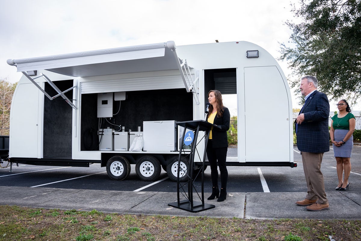 Kelly Stevens speaking in front of the REACH Hub trailer