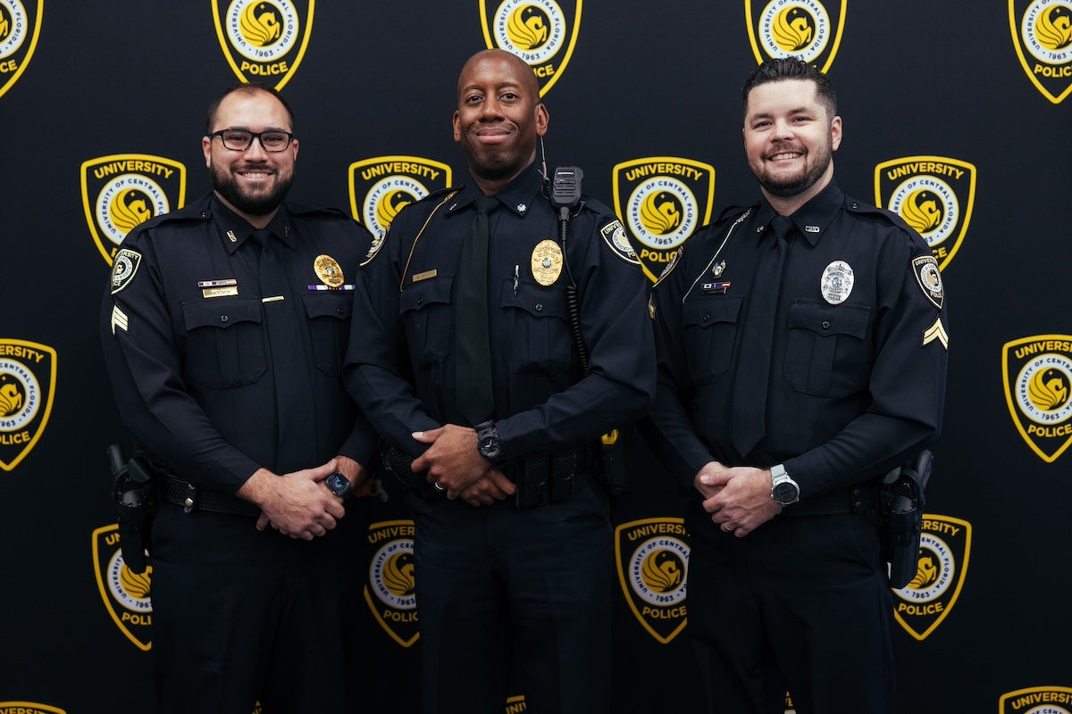 UCF Police Department officers Alexander DeLuca, Matthew Scott and Al Sammelian pose for a photo in front of a backdrop