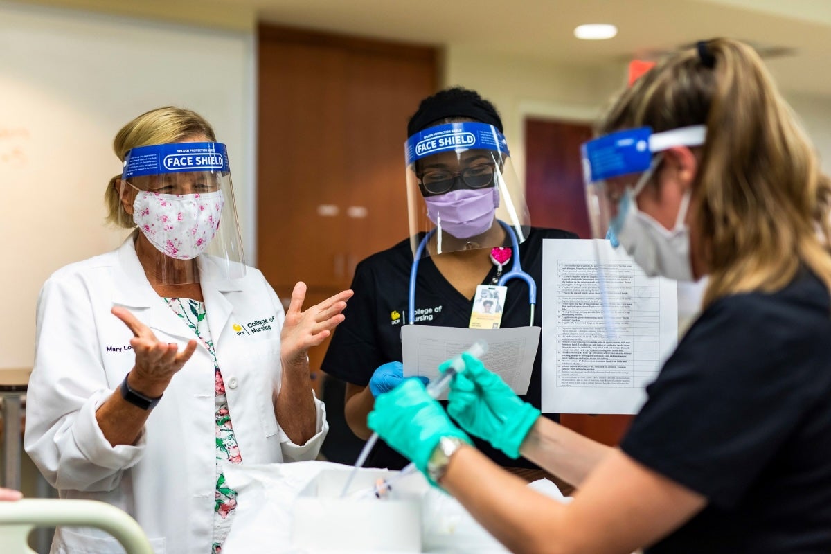 Three people wearing face guards and working with a manikin