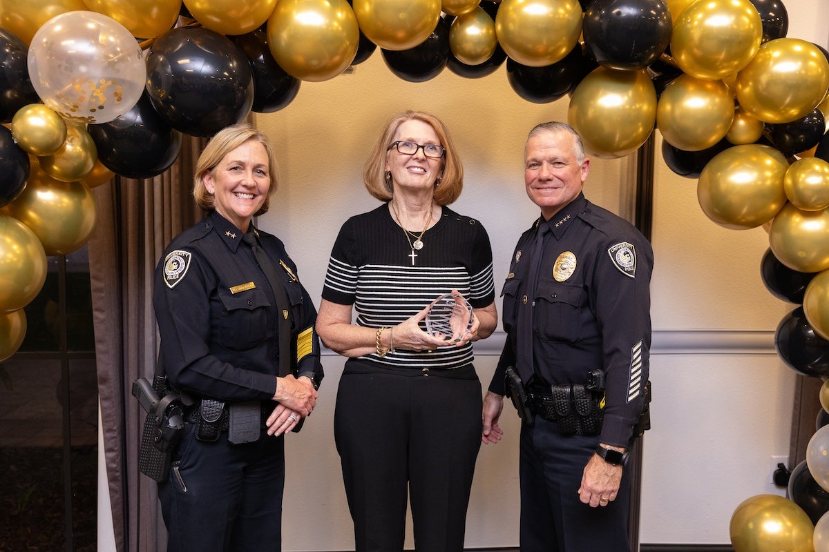 Surrounded by black and gold balloons, Christine Mouton poses for a photo with UCFPD Chief Carl Metzger and Deputy Chief Robin Griffin-Kitzerow