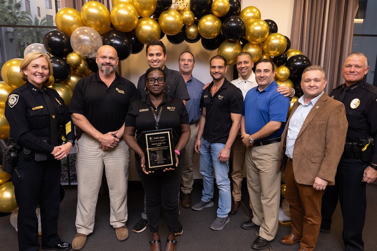 Surrounded by black and gold balloons, members of UCF Public Safety's Administration and Finance Information Technology team pose for a photo with Chief Carl Metzger '03MS and Deputy Chief Robin Griffin-Kitzerow