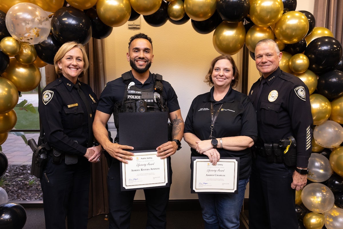 Surrounded by black and gold balloons, Officer Adriel Rivera Aponte, Amber Charles, Chief Carl Metzger and Deputy Chief Robin Griffin-Kitzerow pose together for a photo