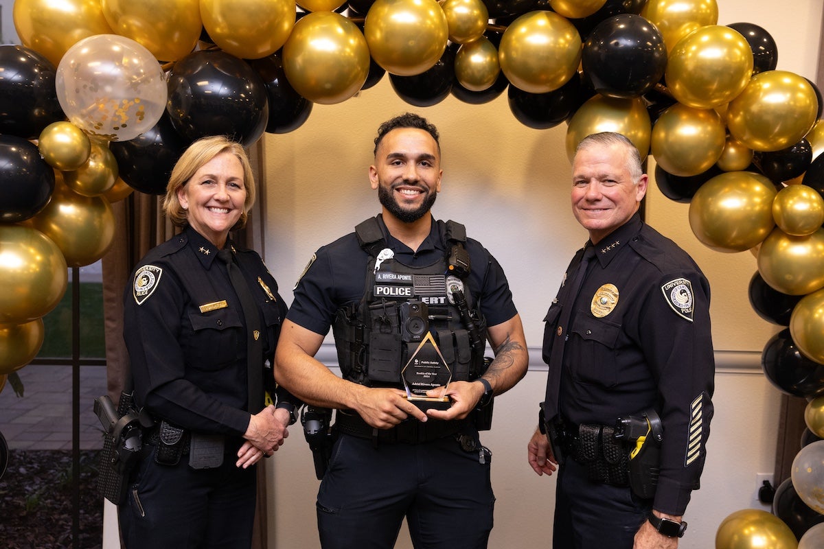 Surrounded by black and gold balloons, Officer Adriel Rivera Aponte poses for a photo with UCFPD Chief Carl Metzger and Deputy Chief Robin Griffin-Kitzerow