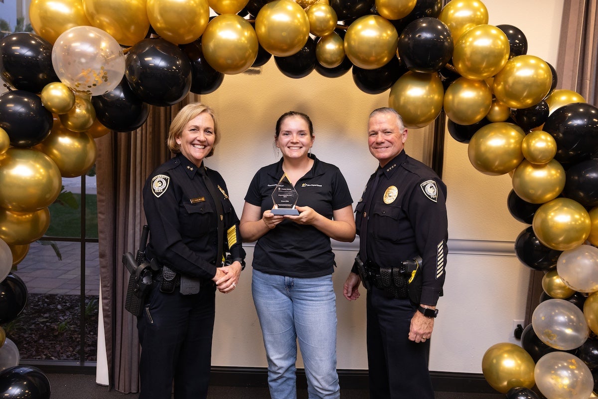 Surrounded by black and gold balloons, Grace Ehle poses for a photo with UCFPD Chief Carl Metzger and Deputy Chief Robin Griffin-Kitzerow