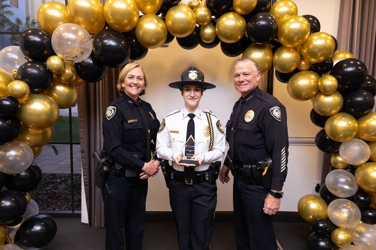 Surrounded by black and gold balloons, Isabella Sanchez poses for a photo with UCFPD Chief Carl Metzger and Deputy Chief Robin Griffin-Kitzerow