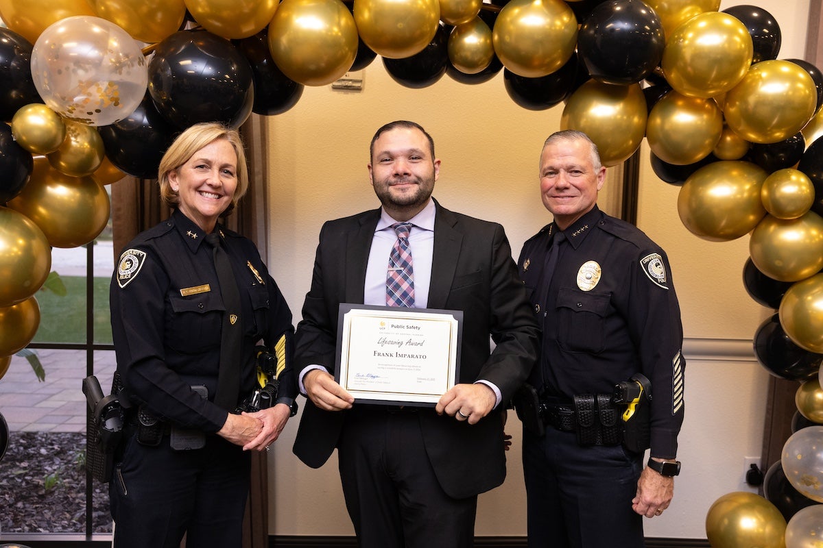 Surrounded by black and gold balloons, Frank Imparato poses for a photo with Chief Carl Metzger and Deputy Chief Robin Griffin-Kitzerow