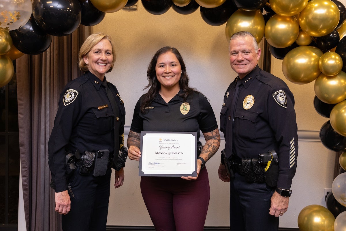 Surrounded by black and gold balloons, Monica Quimbayo poses for a photo with Chief Carl Metzger and Deputy Chief Robin Griffin-Kitzerow