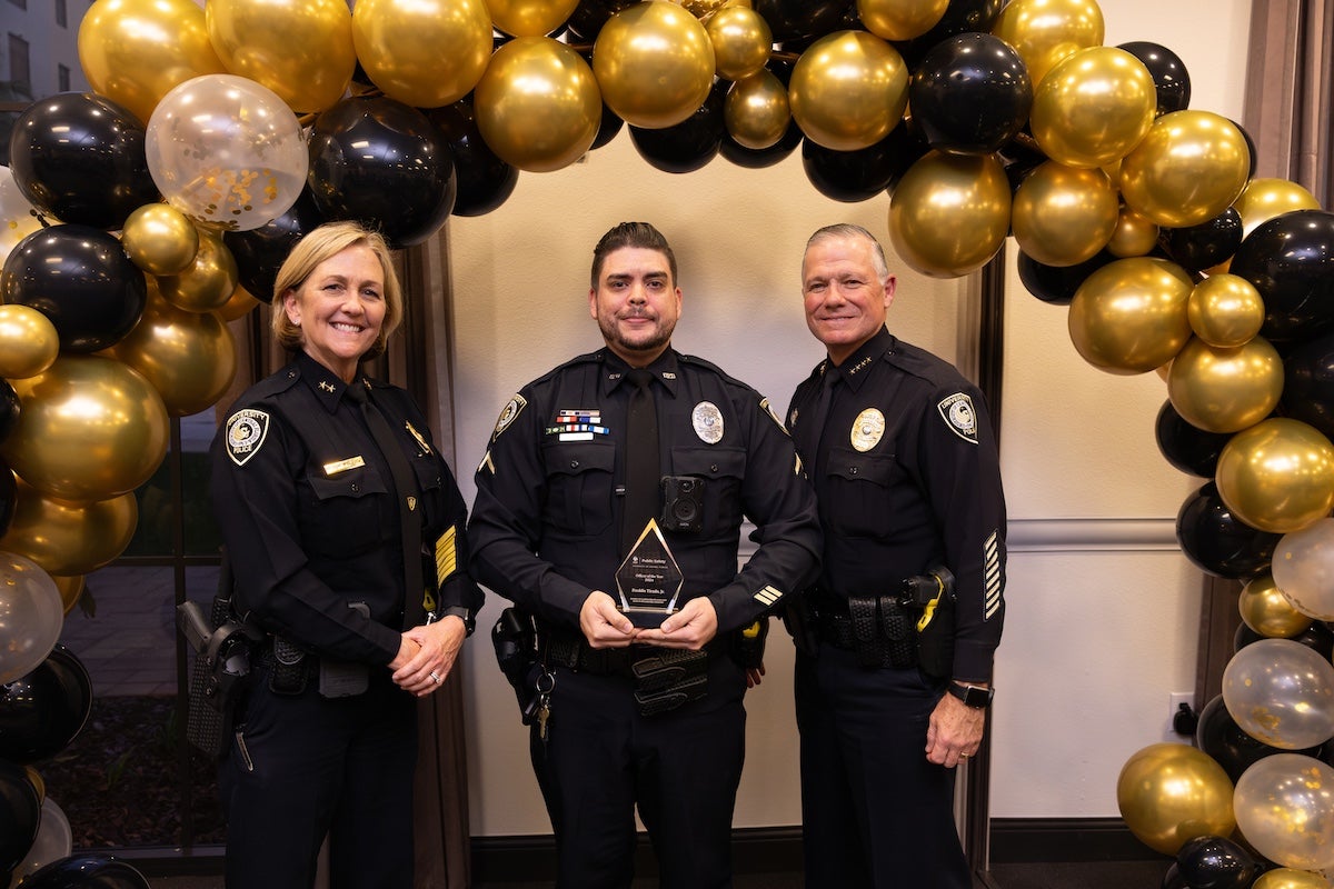 Surrounded by black and gold balloons, UCFPD Officer Freddie Tirado Jr. poses for a photo with UCFPD Chief Carl Metzger and Deputy Chief Robin Griffin-Kitzerow