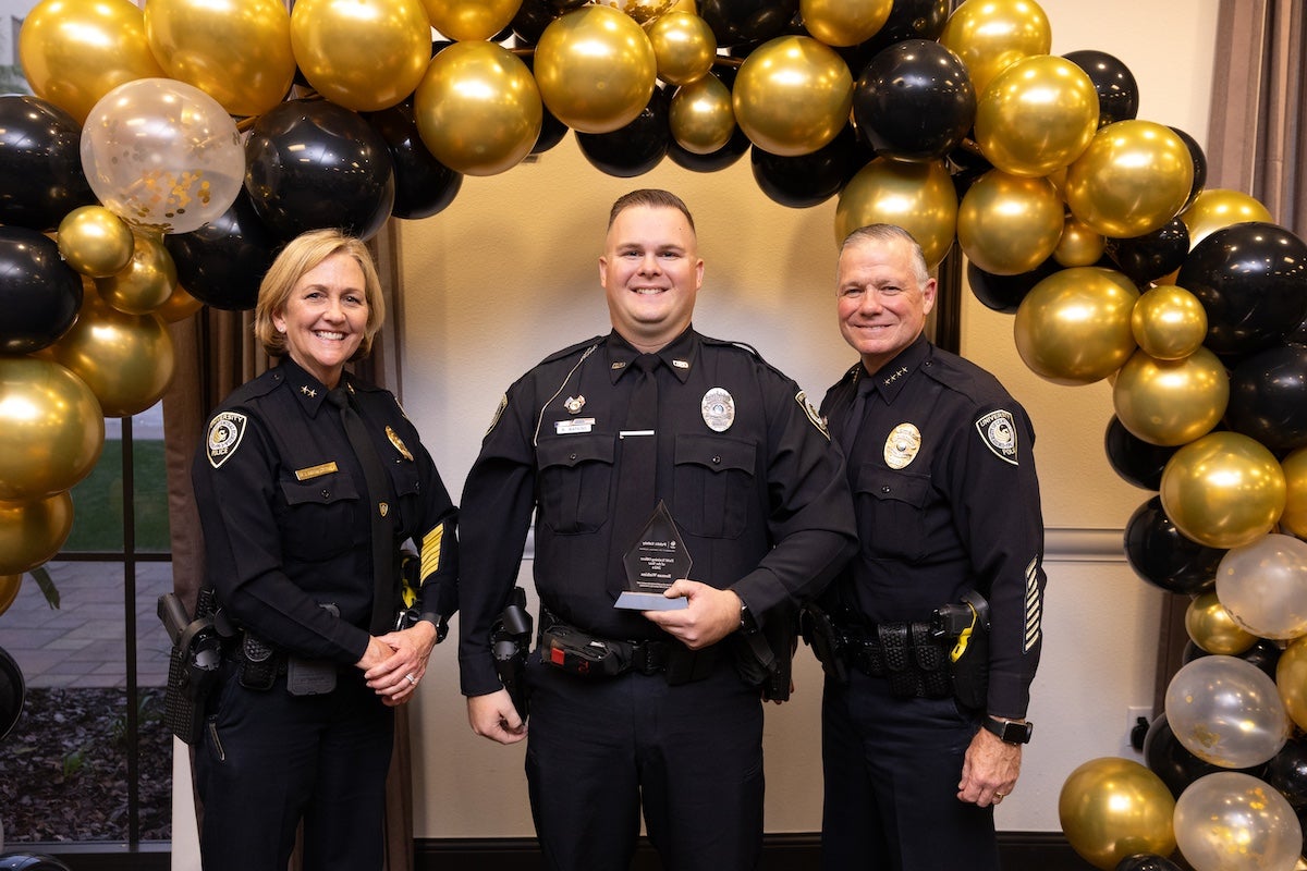 Surrounded by black and gold balloons, Officer Roman Watkins poses for a photo with UCFPD Chief Carl Metzger and Deputy Chief Robin Griffin-Kitzerow