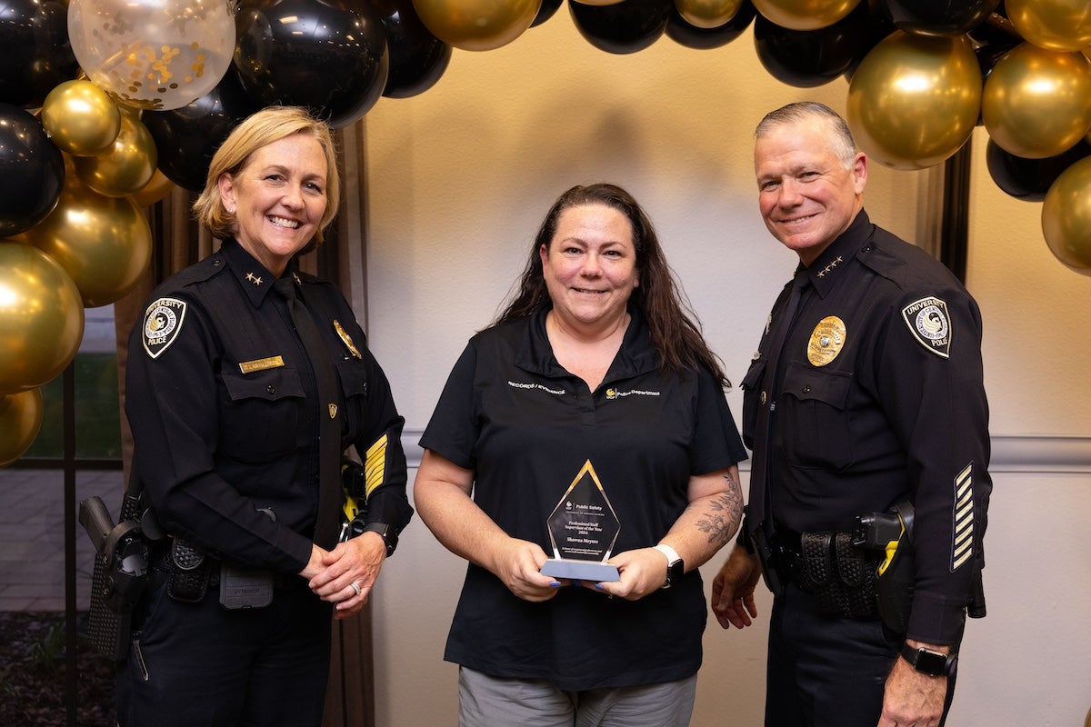 Surrounded by black and gold balloons, Shawna Meyers poses for a photo with UCFPD Chief Carl Metzger and Deputy Chief Robin Griffin-Kitzerow