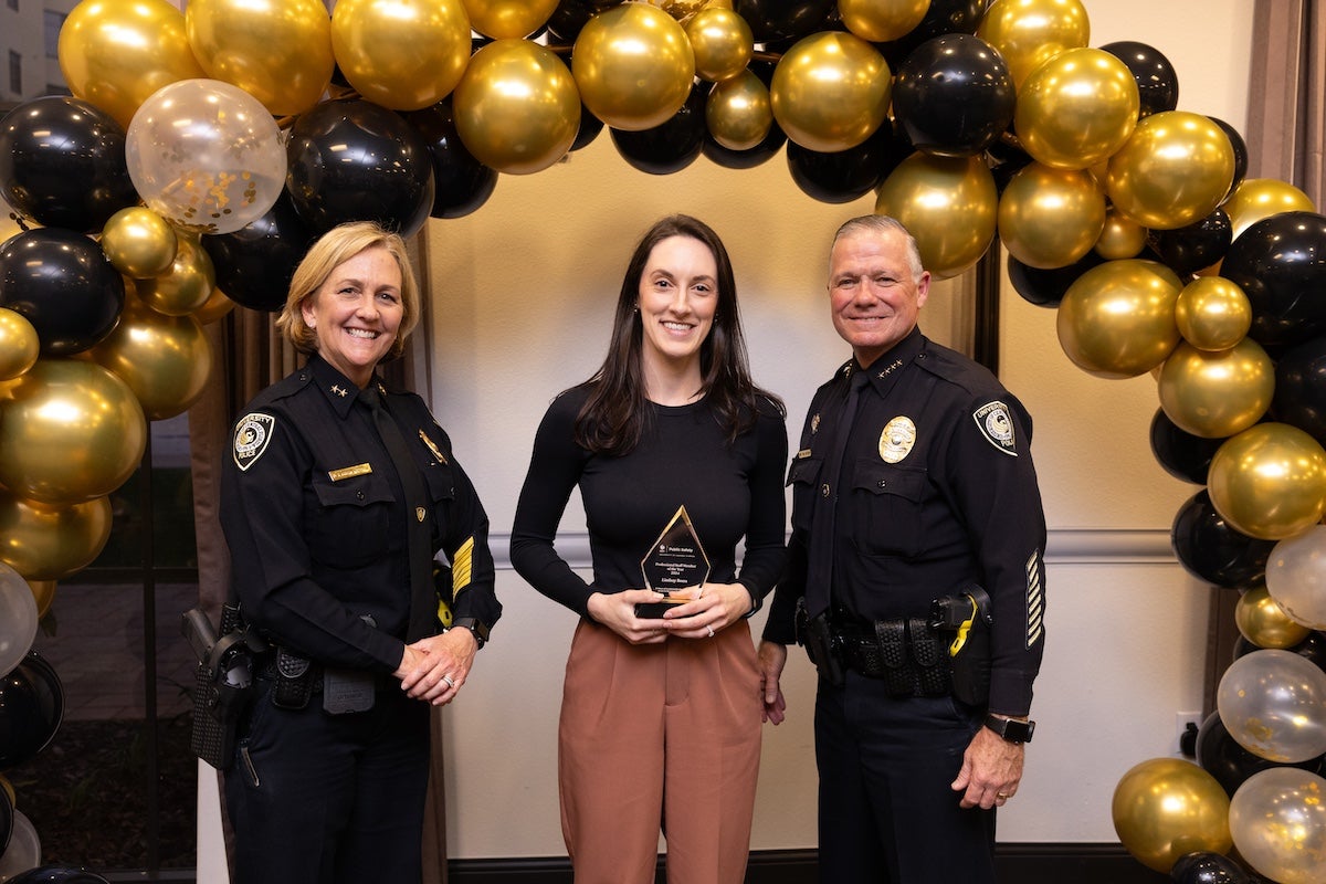 Surrounded by black and gold balloons, Lindsay Beers poses for a photo with UCFPD Chief Carl Metzger and Deputy Chief Robin Griffin-Kitzerow