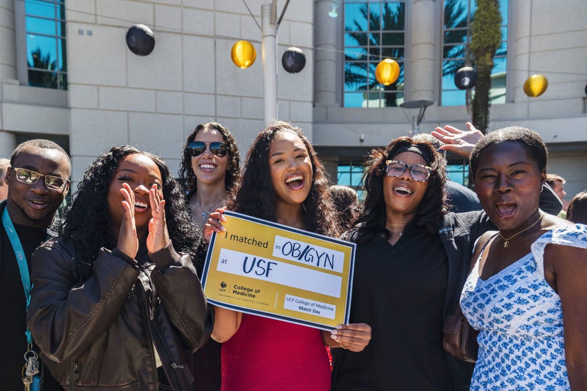 A group of people standing next to a UCF College of Medicine student holding a Match Day sign. 