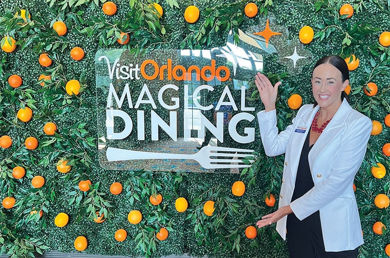 Kristin Rothbauer-Westover pointing the a VisitOrlando Magical Dining sign