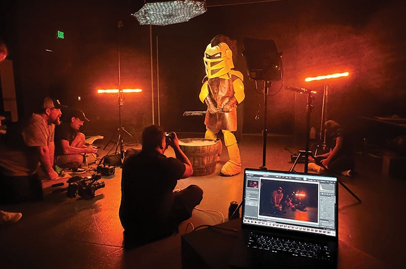 A studio setup with lights, a camera and laptop recording Knightro pulling a license plate out of a blacksmith bucket