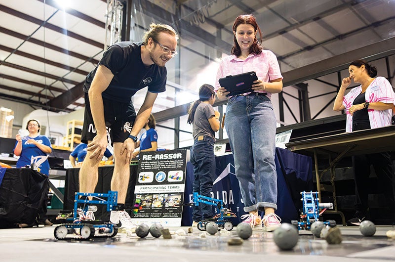 A person watching another use a tablet to move a robot through moon-shaped obstacles