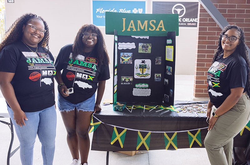 Three students standing in front of a poster board for the JAMSA Student Organization and Jamaican flags