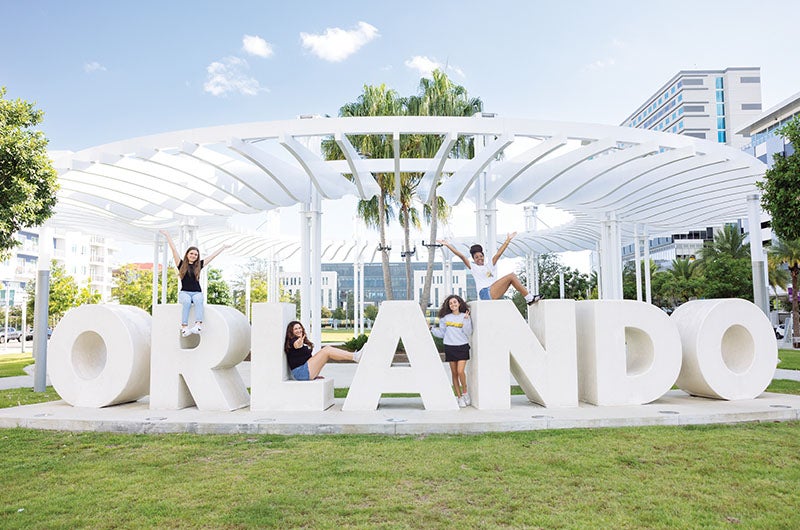 Students standing in and n top of the ORLANDO sign in the downtown area